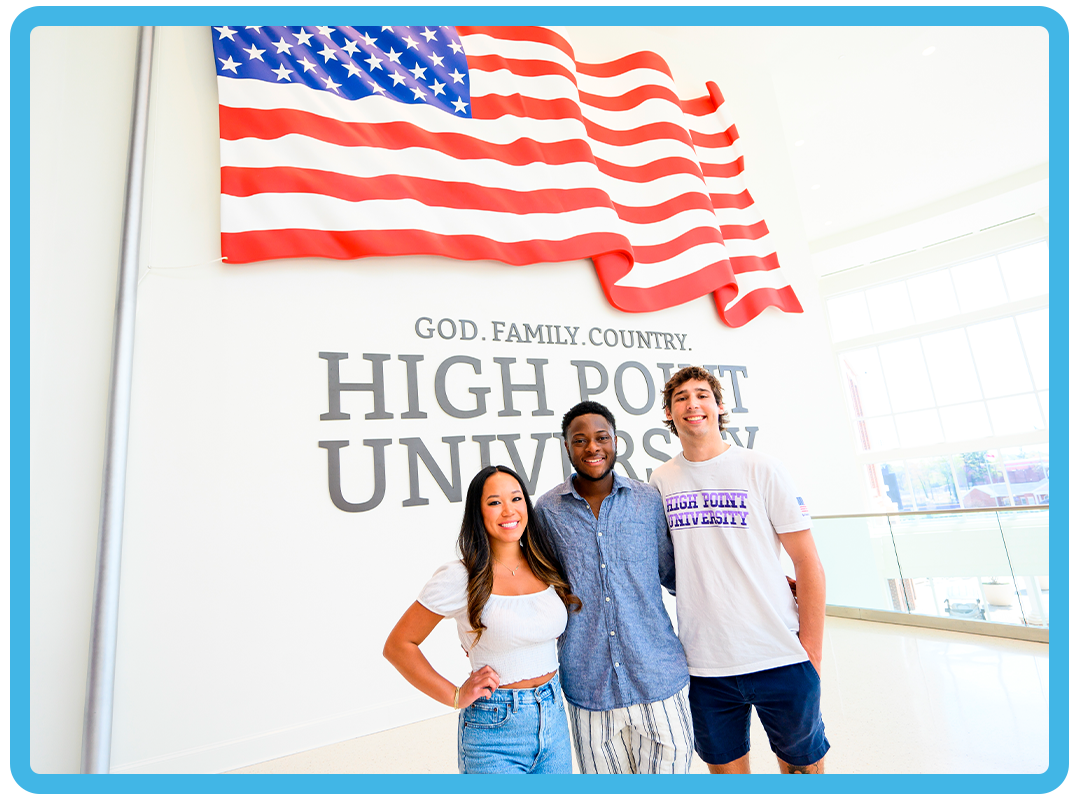 Three students standing in front of a sign that reads High Point University, God, Family, Country.